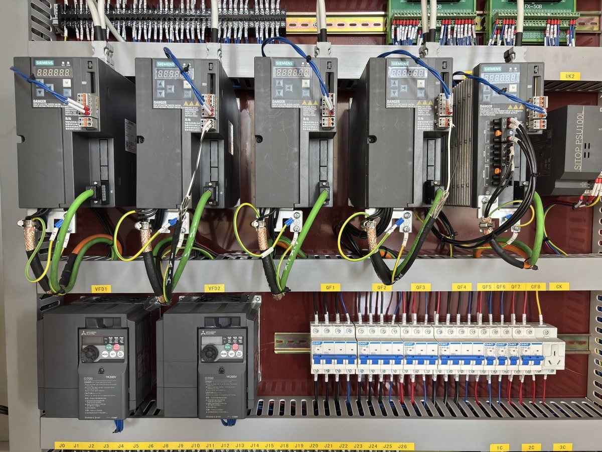 Quality In The Fast Lane (Burr Control) Interior close-up of an industrial electrical control cabinet featuring SIEMENS servo drives and MITSUBISHI ELECTRIC D700 frequency inverters.
